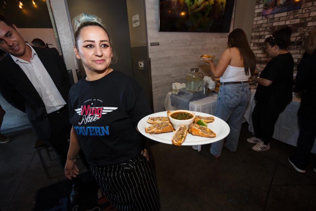 A server works a special event at Wing Nutz Tavern, holding a tray of birria egg rolls